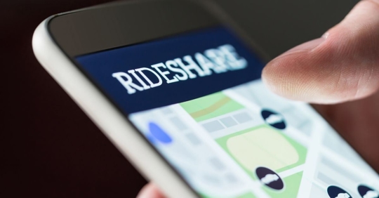 Man holding a phone that has an open rideshare app